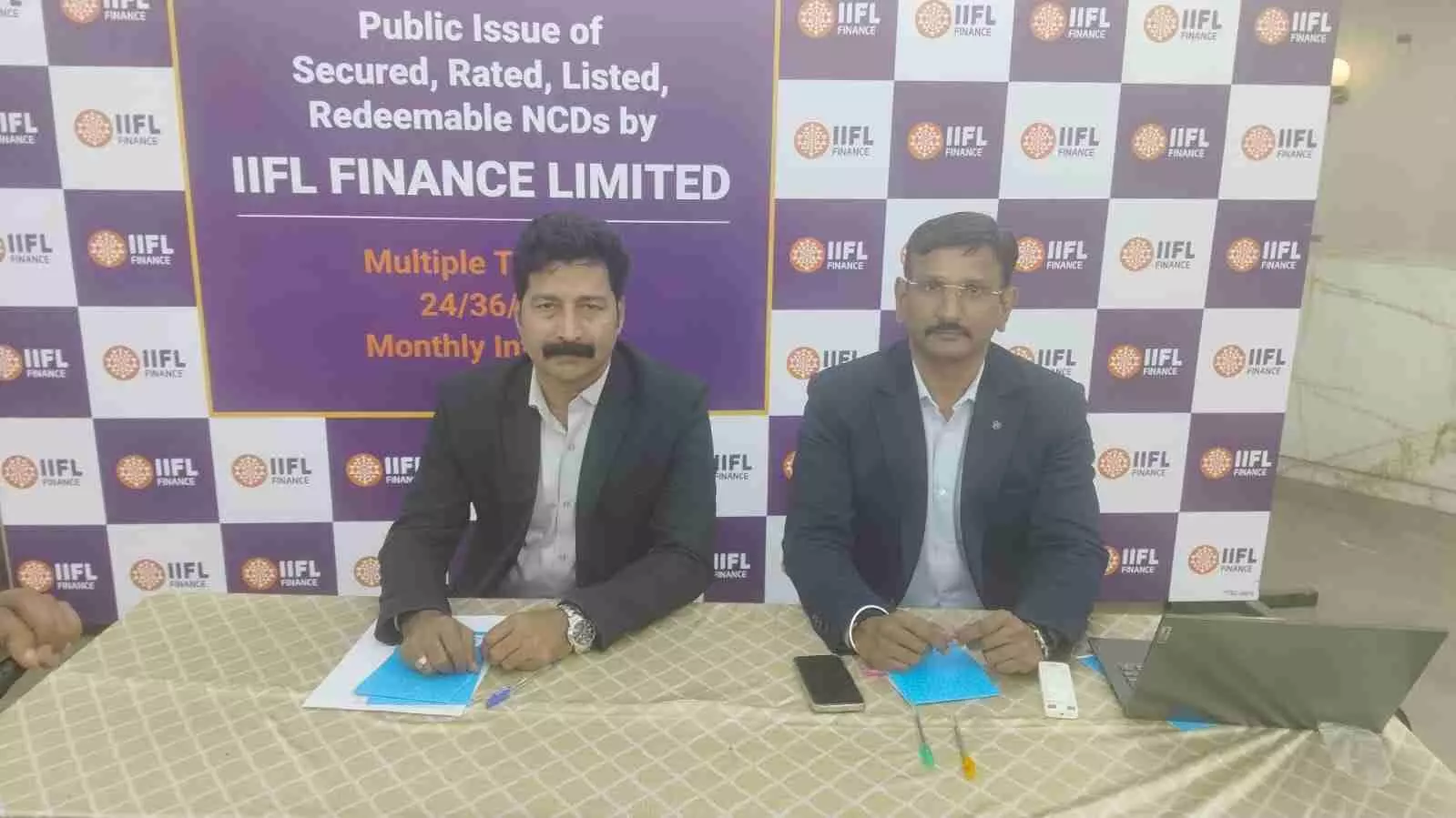 आईआईएफएल फाईनेंस कंपनी का लोगो और निवेश संबंधित दस्तावेज मेज पर रखे हुए दिखाई दे रहे हैं।