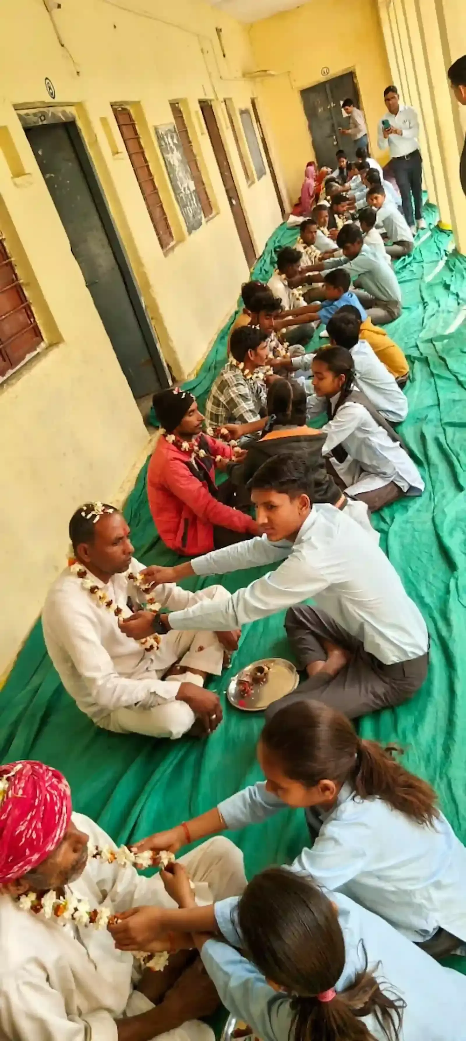 स्कूल में विद्यार्थी अपने माता-पिता और गुरुजनों का तिलक लगाकर पूजन कर रहे हैं।