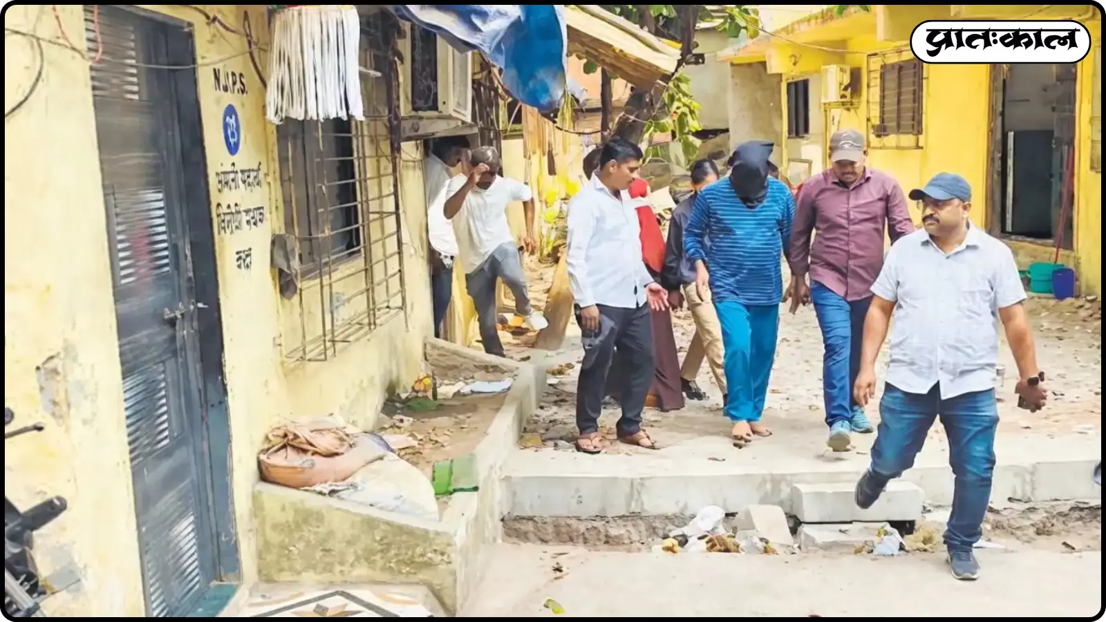 पीली दीवार वाली गली में पुलिसकर्मी एक व्यक्ति को ले जा रहे हैं जिसका सिर काले कपड़े से ढका है। पीली दीवार वाली गली में पुलिसकर्मी एक व्यक्ति को ले जा रहे हैं जिसका सिर काले कपड़े से ढका है।