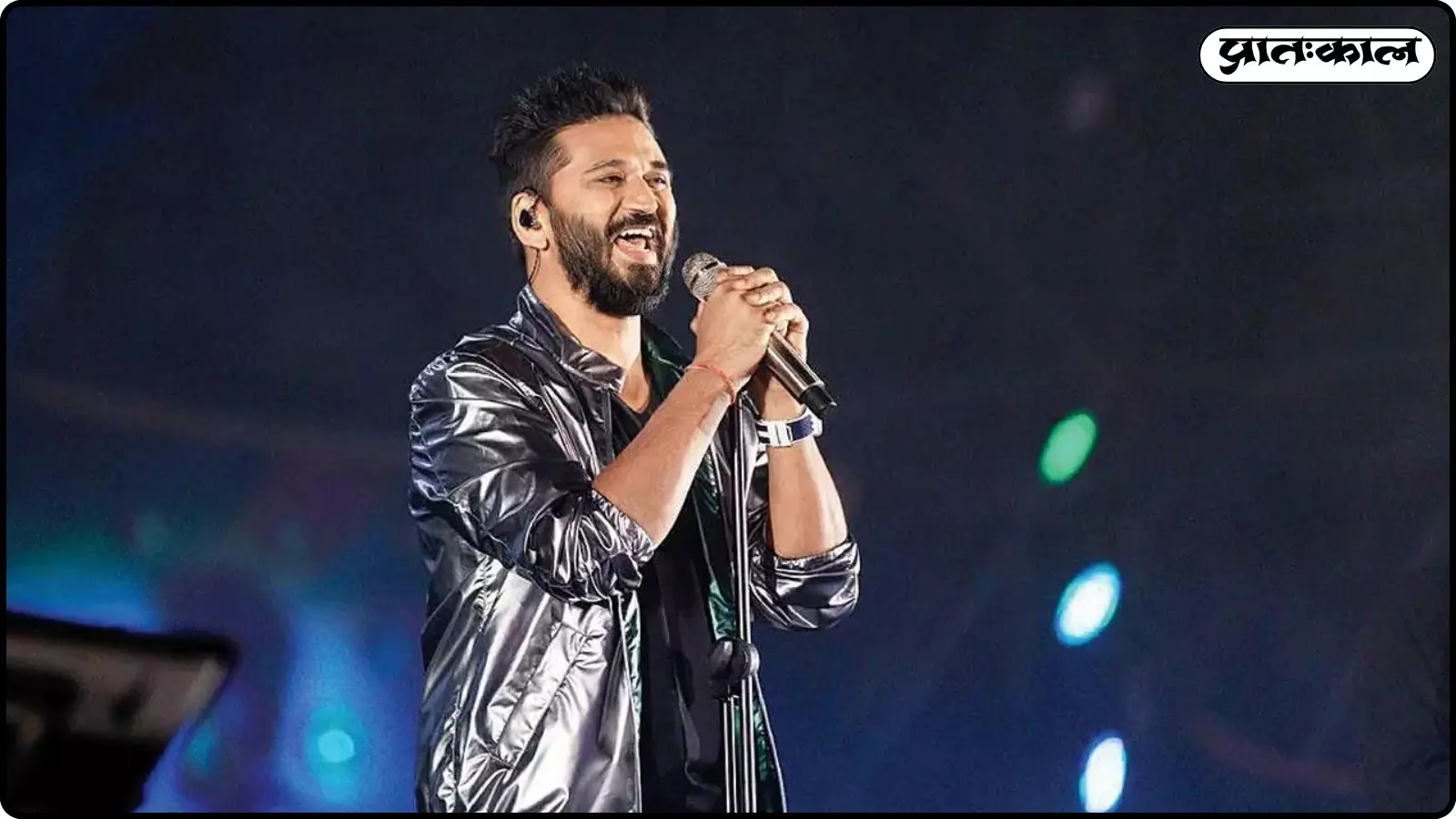 चमकीली सिल्वर जैकेट पहने अमित त्रिवेदी मंच पर माइक पकड़कर मुस्कुराते हुए गाना गा रहे हैं। चमकीली सिल्वर जैकेट पहने अमित त्रिवेदी मंच पर माइक पकड़कर मुस्कुराते हुए गाना गा रहे हैं।