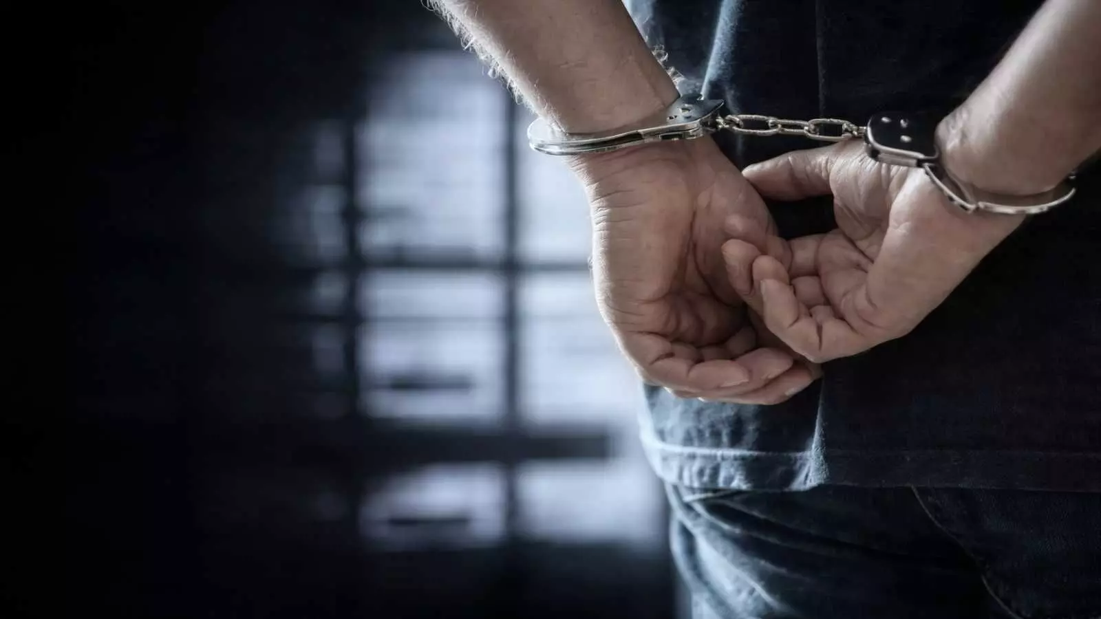 पुलिस कस्टडी में हथकड़ी लगा हुआ एक युवक सुरक्षा जांच के संदर्भ में खड़ा है। पुलिस कस्टडी में हथकड़ी लगा हुआ एक युवक सुरक्षा जांच के संदर्भ में खड़ा है।