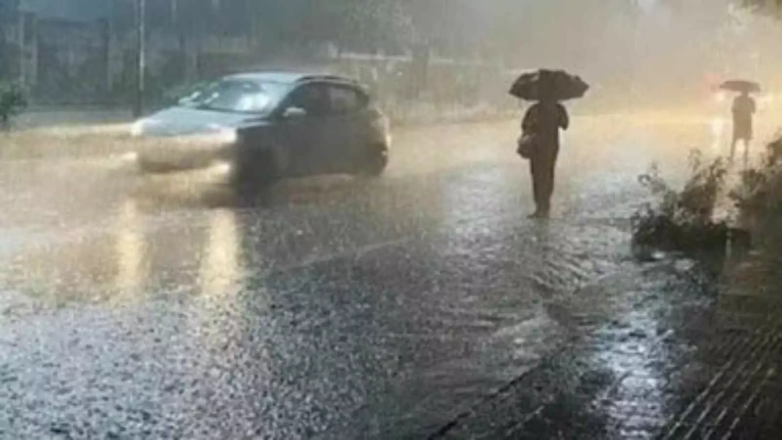 उत्तर प्रदेश की सड़क पर भारी बारिश के बीच छतरी लेकर चलते लोग और वाहन। उत्तर प्रदेश की सड़क पर भारी बारिश के बीच छतरी लेकर चलते लोग और वाहन।