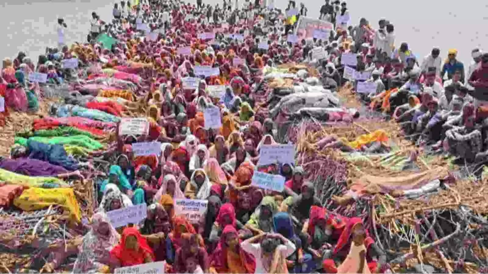 नदी किनारे बड़ी संख्या में महिलाएं विरोध स्वरूप लकड़ियों के ढेर पर लेटी हुई दिखाई दे रही हैं।