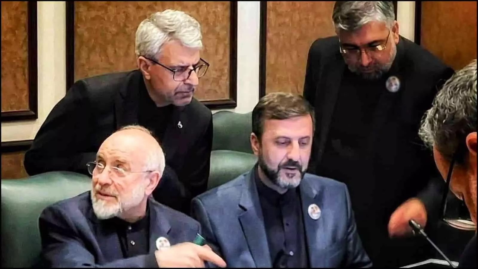 गहरे रंग के सूट पहने ईरानी प्रतिनिधिमंडल के सदस्य मेज पर बैठकर दस्तावेजों और कूटनीतिक प्रस्तावों पर चर्चा कर रहे हैं।