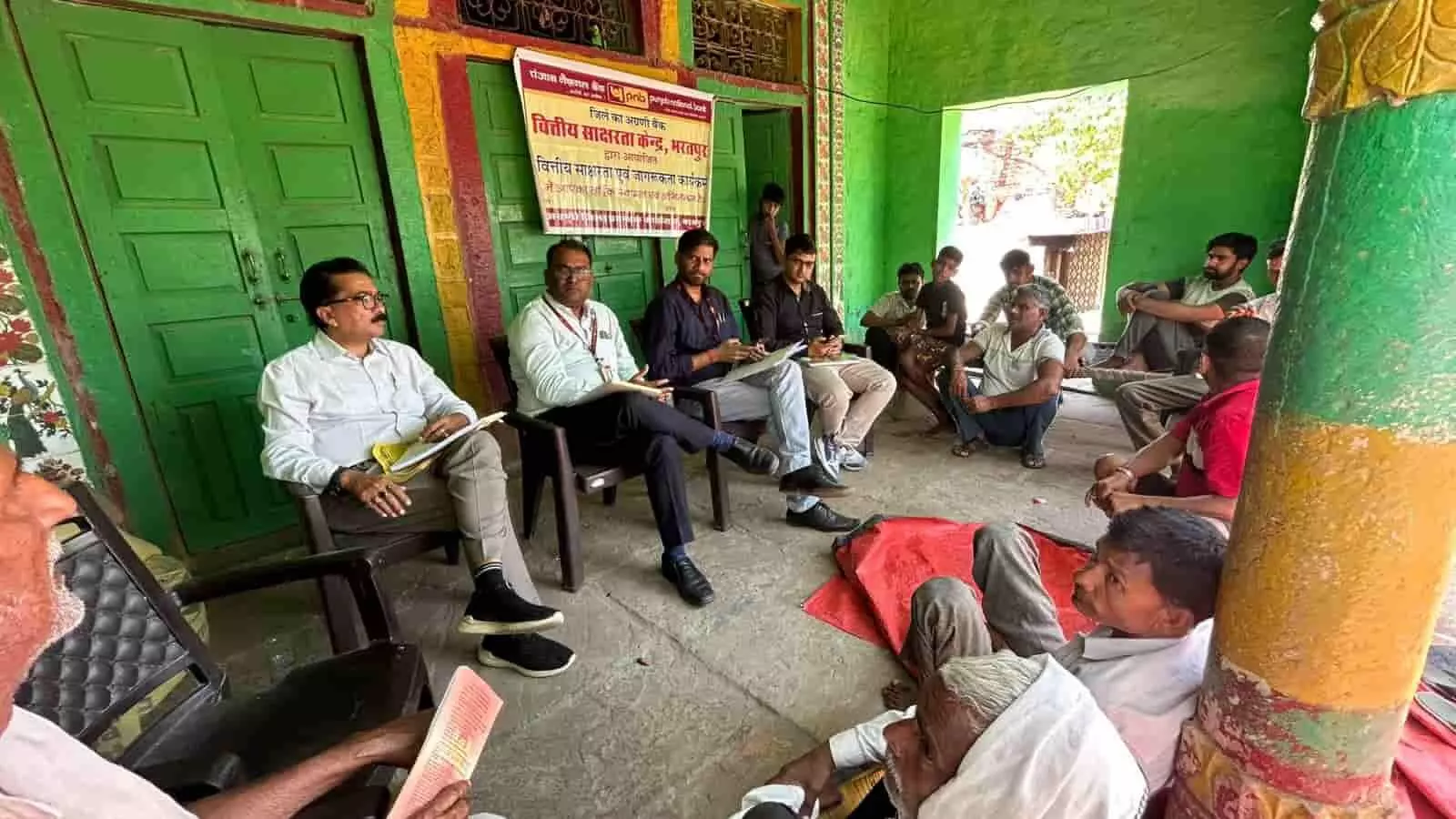 कुर्सियों पर बैठे बैंक अधिकारी और जमीन पर बैठे ग्रामीण वित्तीय जागरूकता कार्यक्रम के दौरान कुर्सियों पर बैठे बैंक अधिकारी और जमीन पर बैठे ग्रामीण वित्तीय जागरूकता कार्यक्रम के दौरान