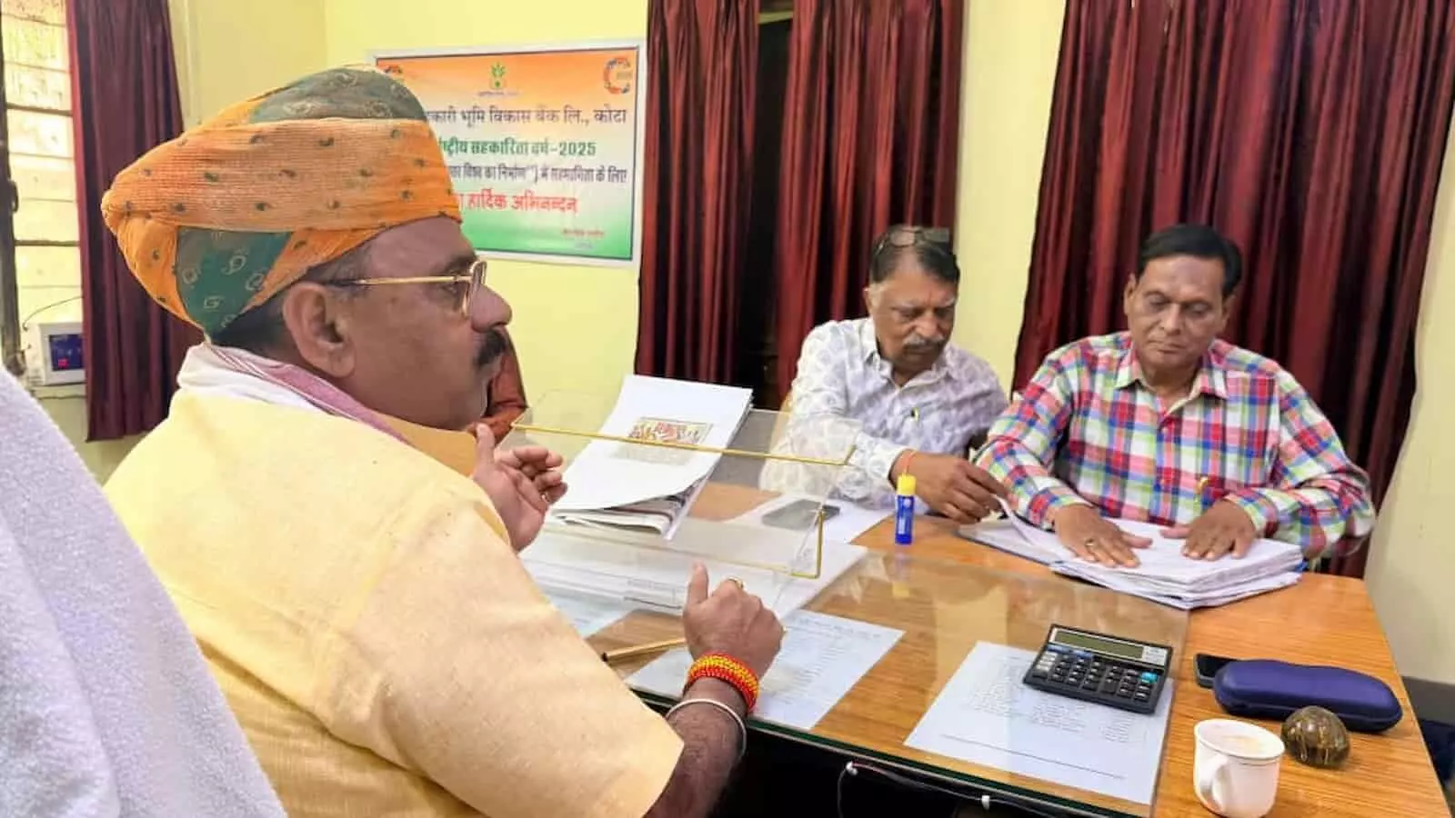 बैंक कार्यालय में मेज पर फाइलें देखते हुए अध्यक्ष चैन सिंह राठौड़ और अन्य बैंक अधिकारी ऋण राहत योजना की समीक्षा कर रहे हैं। बैंक कार्यालय में मेज पर फाइलें देखते हुए अध्यक्ष चैन सिंह राठौड़ और अन्य बैंक अधिकारी ऋण राहत योजना की समीक्षा कर रहे हैं।