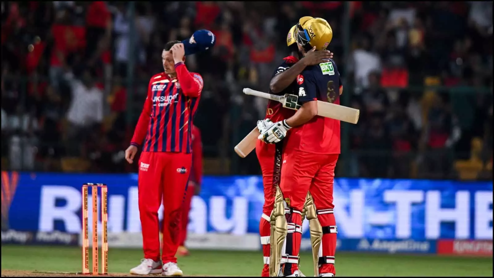 क्रिकेट के मैदान पर एक दूसरे को गले लगाकर जीत की बधाई देते बेंगलुरु के दो खिलाड़ी।