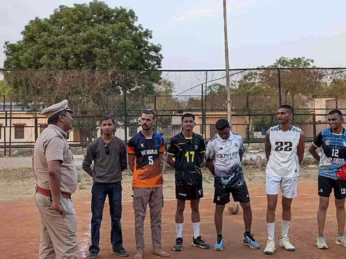 खेल के मैदान पर खड़े पुलिस अधिकारी और वॉलीबॉल प्रतियोगिता में भाग लेने वाले युवा खिलाड़ी।