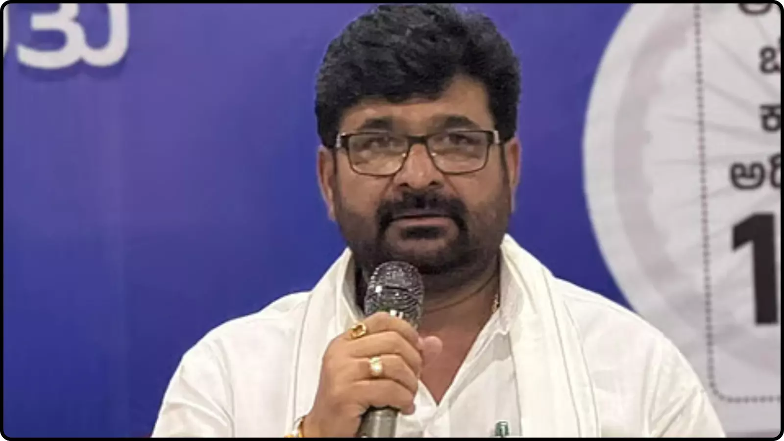 नीले बैकग्राउंड के सामने चश्मा पहने हुए विधायक विनय कुलकर्णी हाथ में माइक्रोफोन लेकर बोल रहे हैं।