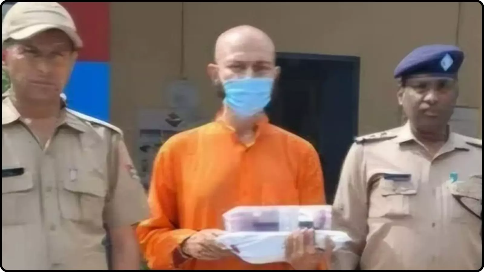 पुलिस कर्मियों के बीच खड़ा भगवा वस्त्र और मास्क पहने संदिग्ध व्यक्ति ऋषिकेश पुलिस स्टेशन के बाहर।