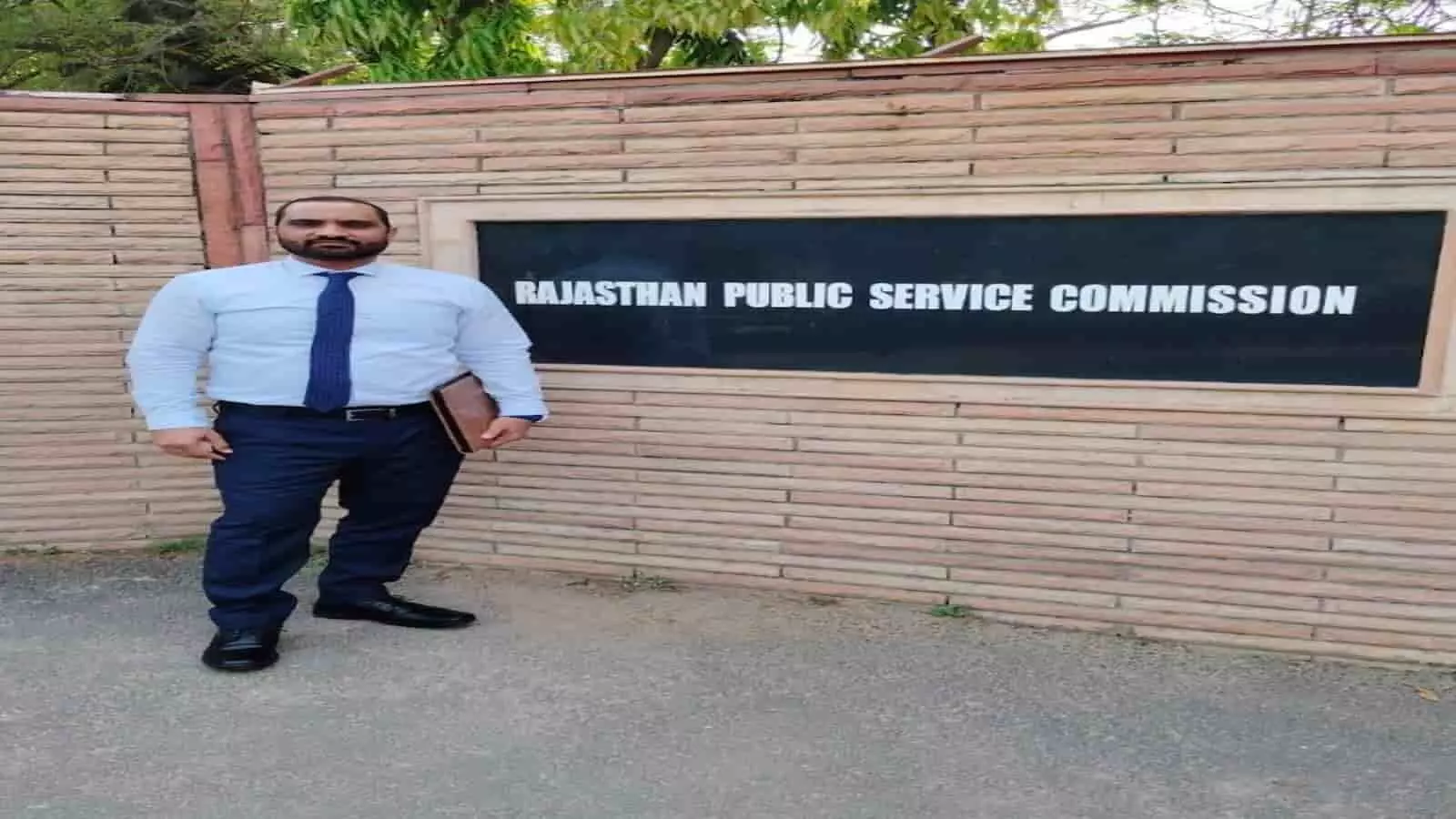 आरपीएससी कार्यालय के बाहर नीली टाई और औपचारिक पोशाक में खड़े विजय सिंह जाट।