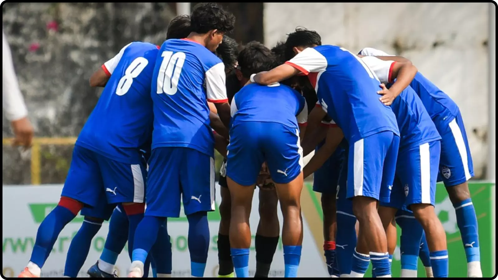 मैदान पर नीली जर्सी पहने फुटबॉल खिलाड़ी एक साथ घेरा बनाकर खड़े हुए गोवा में फाइनल के दौरान।