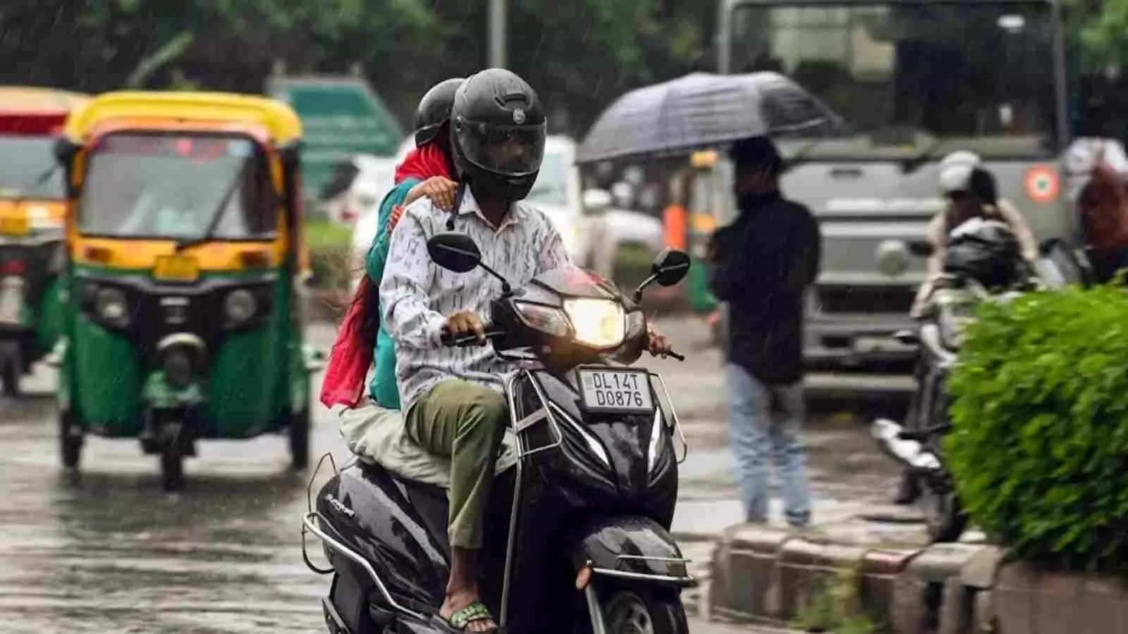 बारिश वाली सड़क पर स्कूटी चलाते हुए दो व्यक्ति और बगल में चलते पीले रंग के ऑटो। बारिश वाली सड़क पर स्कूटी चलाते हुए दो व्यक्ति और बगल में चलते पीले रंग के ऑटो।
