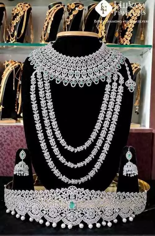 काले स्टैंड पर प्रदर्शित सफेद धातु और हरे रत्न जड़ित हार और झुमके। काले स्टैंड पर प्रदर्शित सफेद धातु और हरे रत्न जड़ित हार और झुमके।
