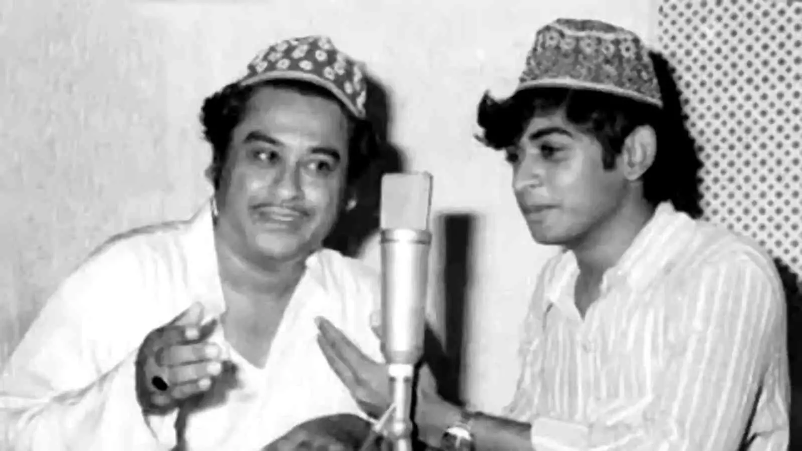 गायक किशोर कुमार और अमित कुमार स्टूडियो में माइक के सामने खड़े होकर गाना गा रहे हैं। गायक किशोर कुमार और अमित कुमार स्टूडियो में माइक के सामने खड़े होकर गाना गा रहे हैं।