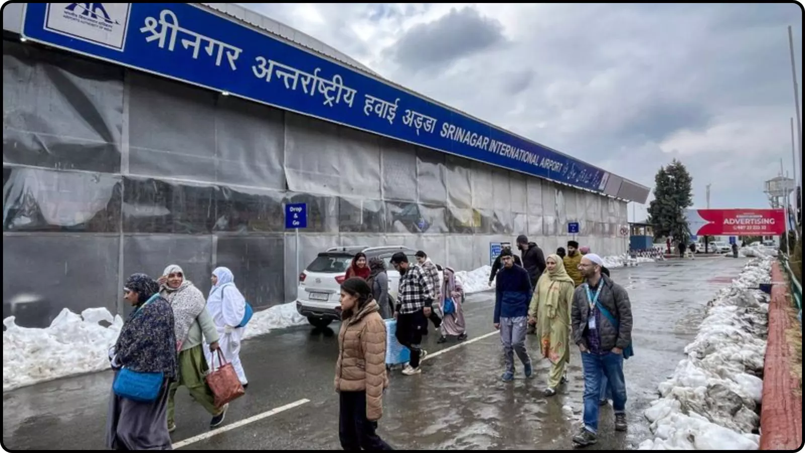 श्रीनगर अंतरराष्ट्रीय हवाईअड्डे के बाहर यात्री और सुरक्षा बोर्ड जांच के संदर्भ में दिखाई दे रहे हैं।