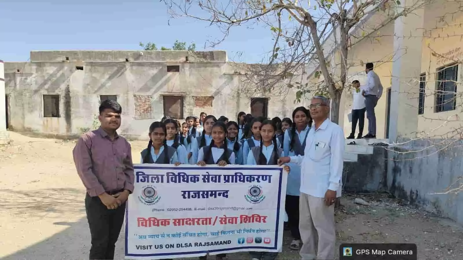 आमेट के स्कूल में जिला विधिक सेवा प्राधिकरण का बैनर पकड़े छात्र और विधिक स्वयंसेवक।