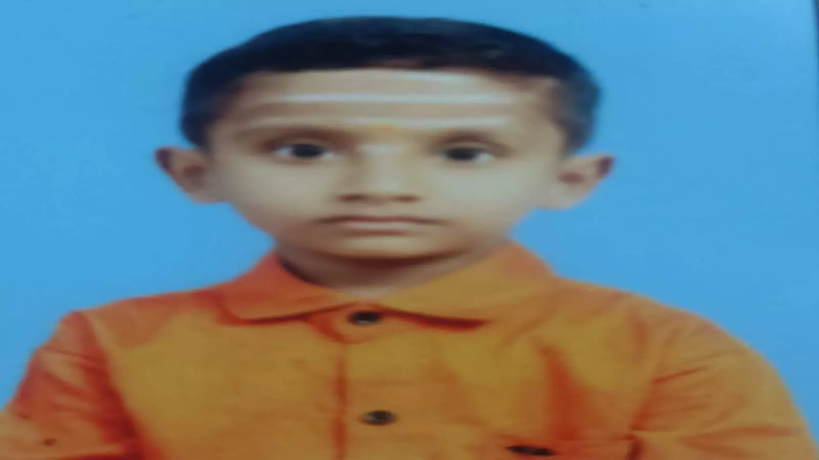 नीली पृष्ठभूमि के सामने नारंगी शर्ट पहने हुए मृत बालक देवांश स्वामी की तस्वीर।