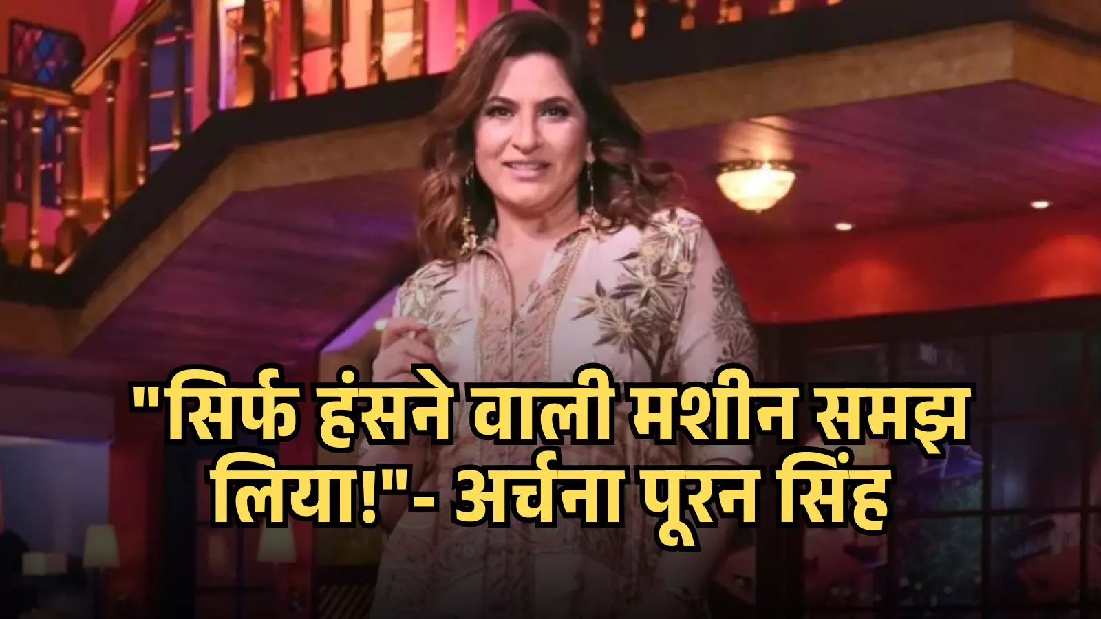 गुलाबी रंग के परिधान में मुस्कुराती हुई अर्चना पूरन सिंह एक सेट के सामने खड़ी दिख रही हैं।