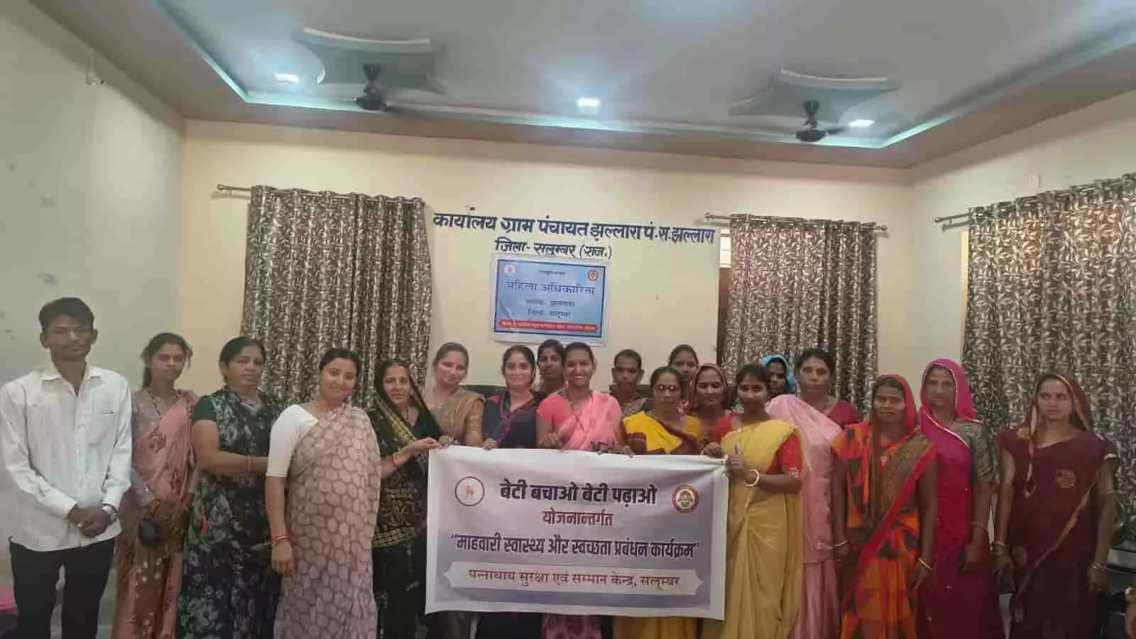 झल्लारा ग्राम पंचायत कार्यालय में बैनर थामे महिलाएं और अधिकारी माहवारी स्वच्छता जागरूकता कार्यक्रम के दौरान।