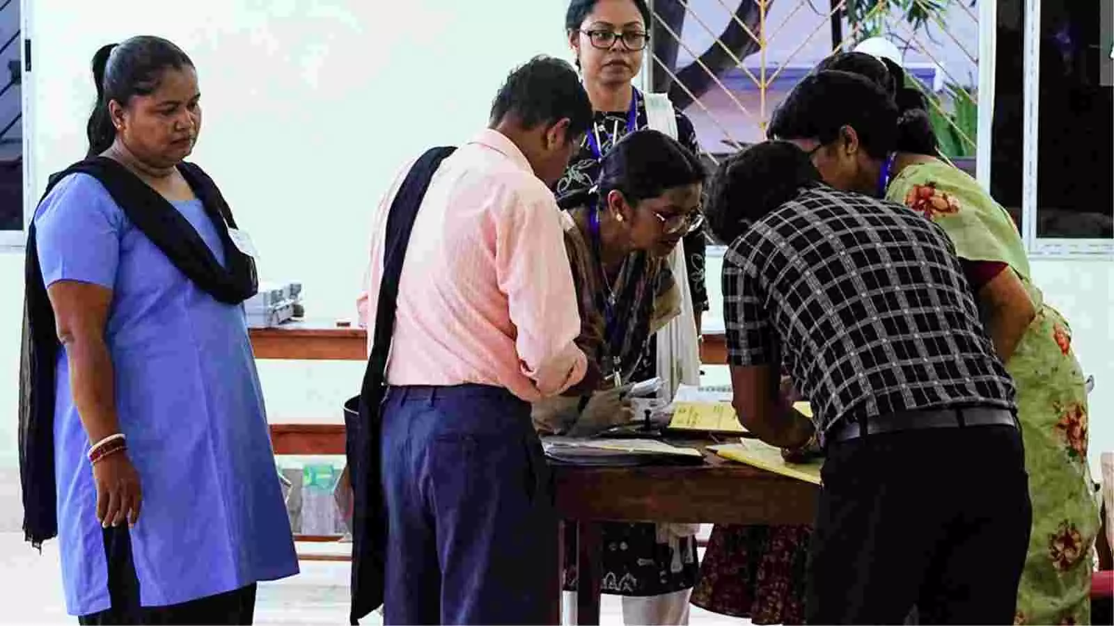 पश्चिम बंगाल के पोलिंग बूथ पर मतदान अधिकारी और वोट देने आए नागरिक कतार में।