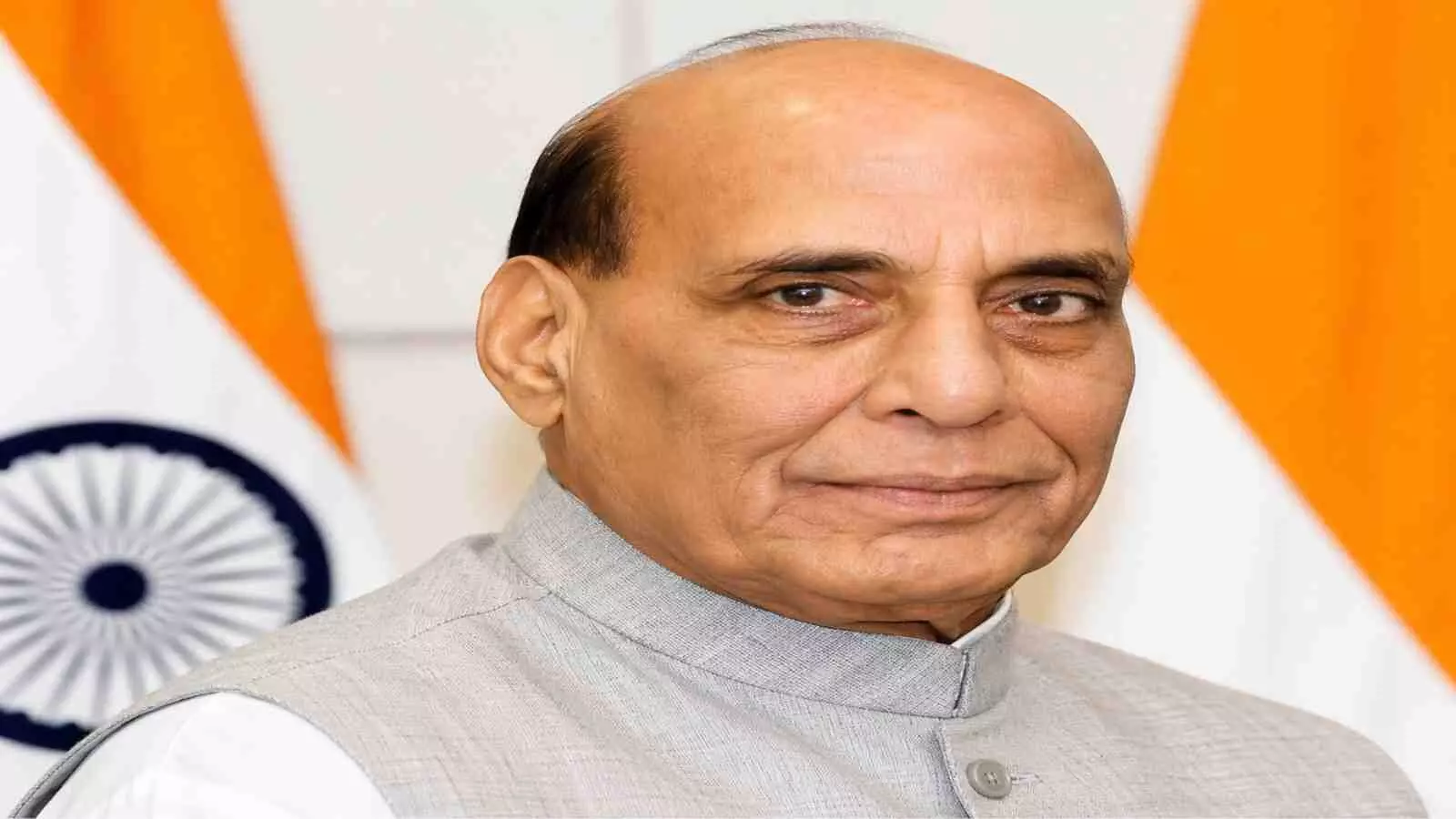 सफेद कुर्ता और जैकेट पहने हुए रक्षा मंत्री राजनाथ सिंह भारतीय तिरंगे के सामने खड़े हैं। सफेद कुर्ता और जैकेट पहने हुए रक्षा मंत्री राजनाथ सिंह भारतीय तिरंगे के सामने खड़े हैं।