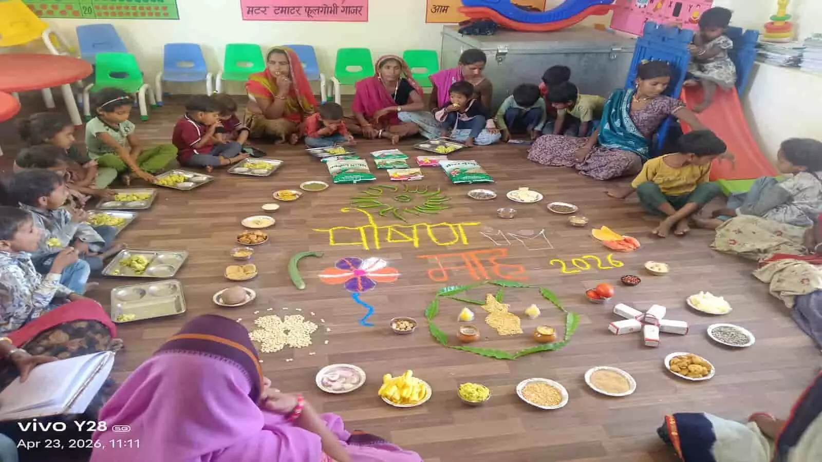 बलीचा के नंदघर में जमीन पर सजे पौष्टिक आहार के साथ बैठे बच्चे और महिलाएं। बलीचा के नंदघर में जमीन पर सजे पौष्टिक आहार के साथ बैठे बच्चे और महिलाएं।