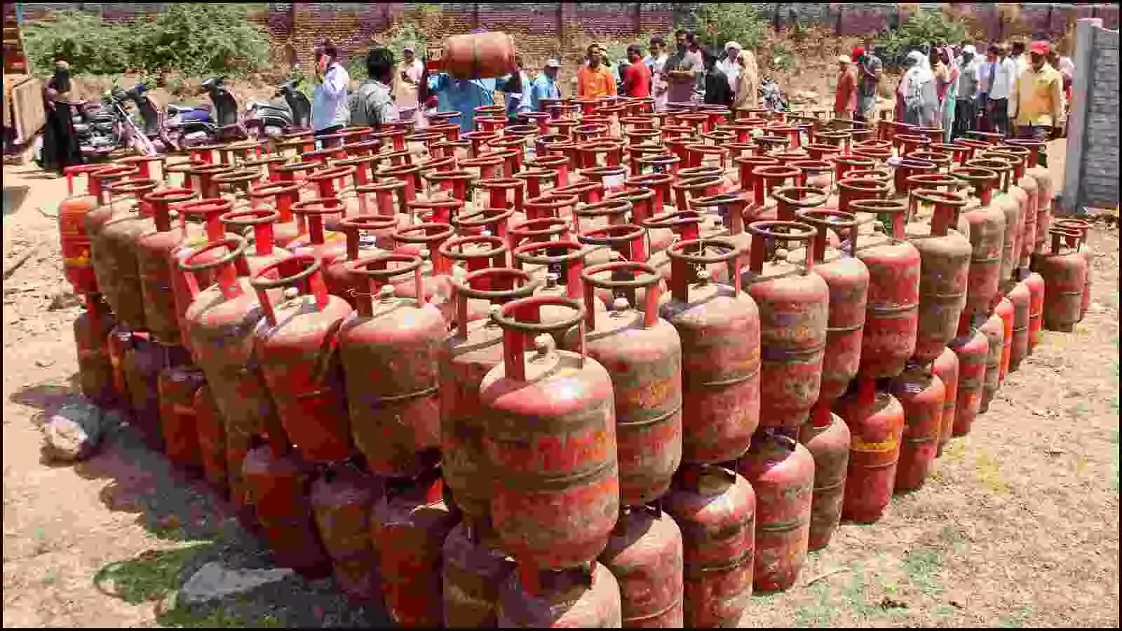 गैस एजेंसी के बाहर मैदान में रखे गए लाल रंग के घरेलू रसोई गैस सिलेंडर और वहां मौजूद लोग। गैस एजेंसी के बाहर मैदान में रखे गए लाल रंग के घरेलू रसोई गैस सिलेंडर और वहां मौजूद लोग।