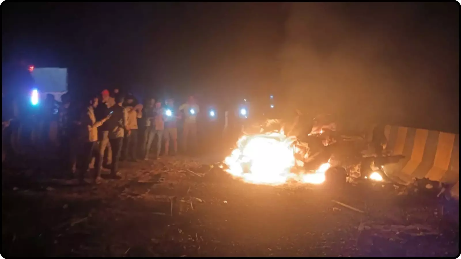 रात के समय सड़क पर जलता हुआ वाहन और पास खड़े लोग मिर्जापुर सड़क हादसे के दौरान। रात के समय सड़क पर जलता हुआ वाहन और पास खड़े लोग मिर्जापुर सड़क हादसे के दौरान।