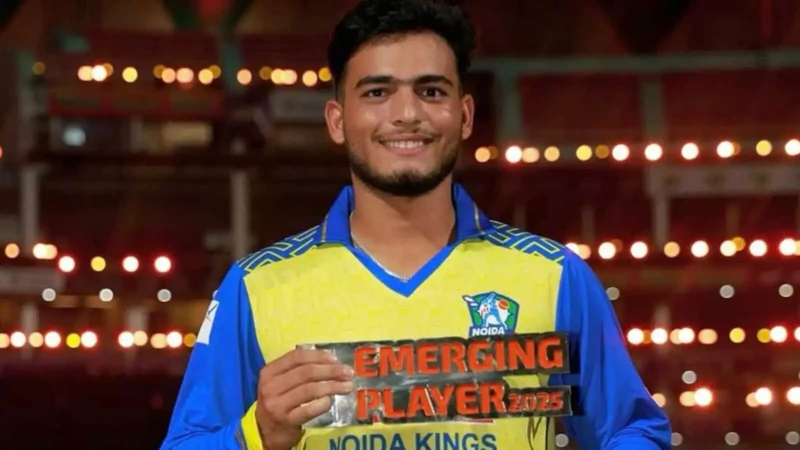 क्रिकेट स्टेडियम में नोएडा किंग्स की जर्सी पहने और इमर्जिंग प्लेयर ट्रॉफी पकड़े हुए प्रशांत रमेंद्र वीर। क्रिकेट स्टेडियम में नोएडा किंग्स की जर्सी पहने और इमर्जिंग प्लेयर ट्रॉफी पकड़े हुए प्रशांत रमेंद्र वीर।
