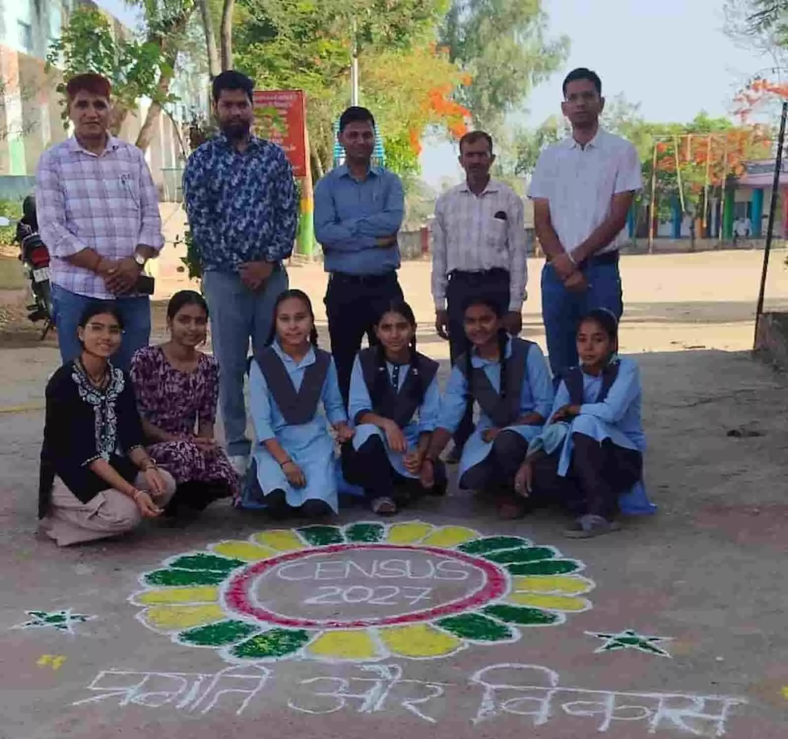 लसाडिया के महात्मा गांधी स्कूल में जनगणना जागरूकता रंगोली के साथ खड़े शिक्षक और छात्राएं।