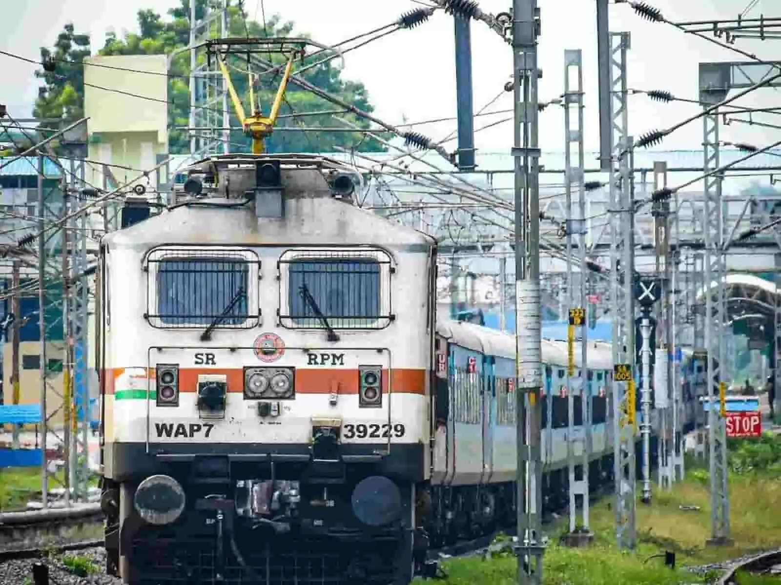 रेलवे ट्रैक पर बिजली के तारों के नीचे खड़ी भारतीय रेल की इलेक्ट्रिक लोकोमोटिव ट्रेन।