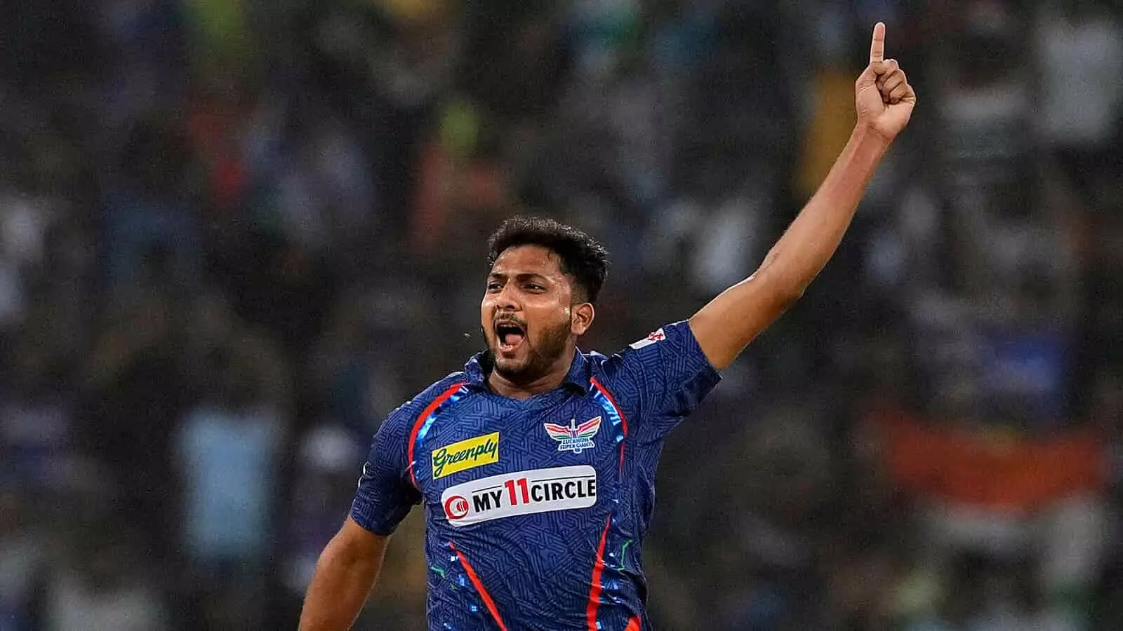 क्रिकेट के मैदान पर नीली जर्सी पहने गेंदबाज मोहसिन खान उंगली उठाकर विकेट का जश्न मना रहे हैं। क्रिकेट के मैदान पर नीली जर्सी पहने गेंदबाज मोहसिन खान उंगली उठाकर विकेट का जश्न मना रहे हैं।