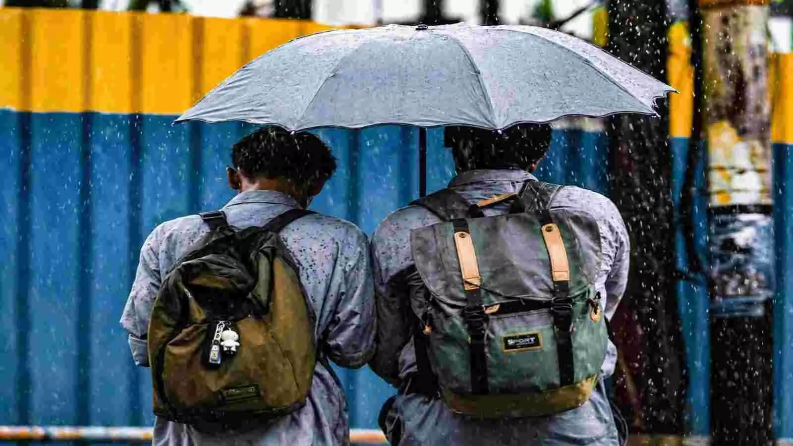 बारिश में छाता लेकर चलते दो युवक जिनके कंधों पर बैग टंगे हैं। बारिश में छाता लेकर चलते दो युवक जिनके कंधों पर बैग टंगे हैं।