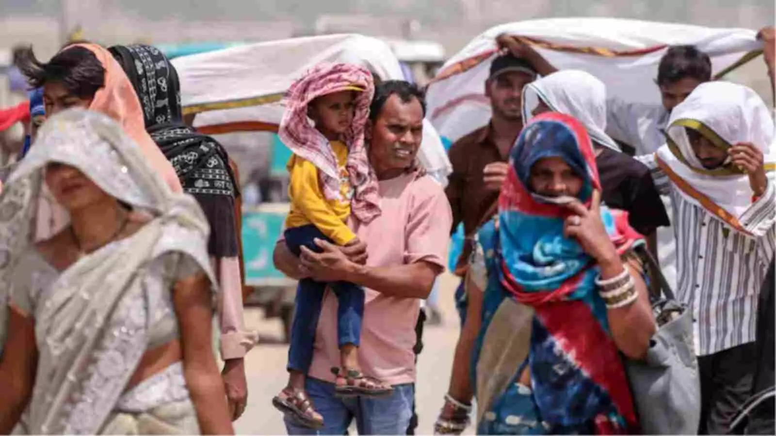 सफेद और रंगीन कपड़ों से अपना चेहरा ढंककर धूप में पैदल चलते हुए लोग दिख रहे हैं।