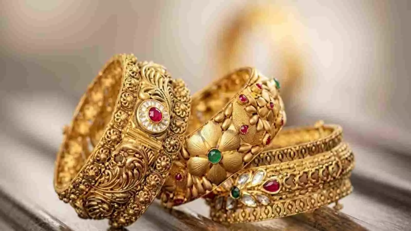 मेज पर रखे हुए सुनहरे नक्काशीदार कंगन भारत में सोने की कीमतों के संदर्भ में| मेज पर रखे हुए सुनहरे नक्काशीदार कंगन भारत में सोने की कीमतों के संदर्भ में|