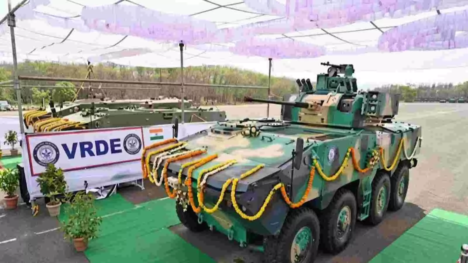फूलों की माला से सजा हुआ पहियों वाला हरे रंग का सैन्य वाहन प्रदर्शन के लिए खड़ा दिख रहा है। फूलों की माला से सजा हुआ पहियों वाला हरे रंग का सैन्य वाहन प्रदर्शन के लिए खड़ा दिख रहा है।