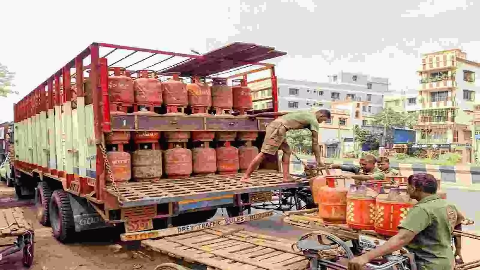 लाल रंग के गैस सिलेंडर से भरा ट्रक और सिलेंडर उतारते कर्मचारी। लाल रंग के गैस सिलेंडर से भरा ट्रक और सिलेंडर उतारते कर्मचारी।