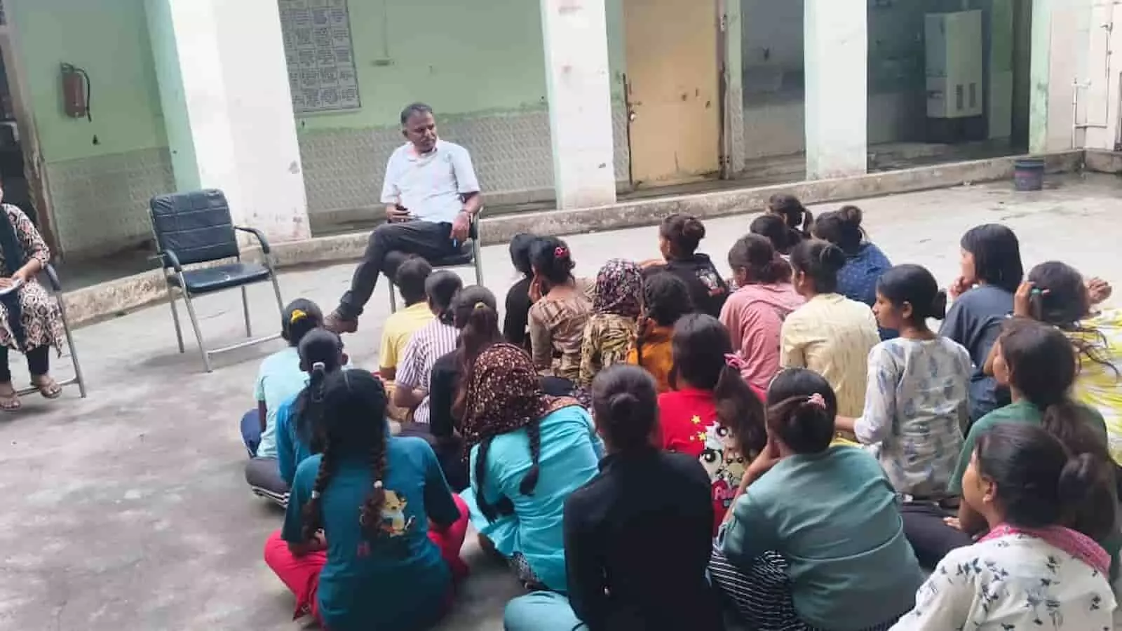खुले प्रांगण में जमीन पर बैठे विद्यार्थियों को संबोधित करते हुए एक अधिकारी। खुले प्रांगण में जमीन पर बैठे विद्यार्थियों को संबोधित करते हुए एक अधिकारी।