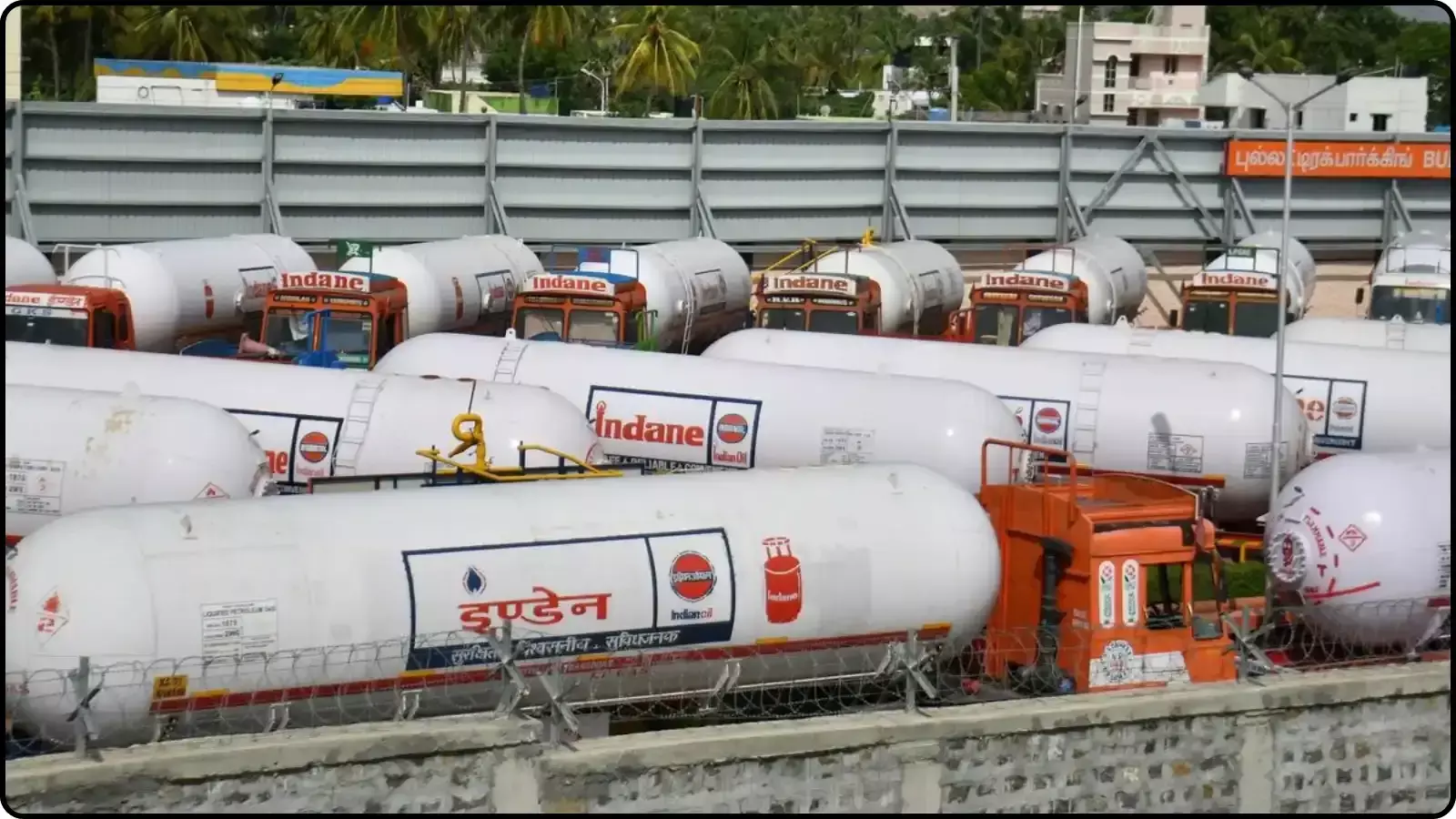 एक कतार में खड़े हुए सफेद और नारंगी रंग के कई एलपीजी गैस टैंकर।