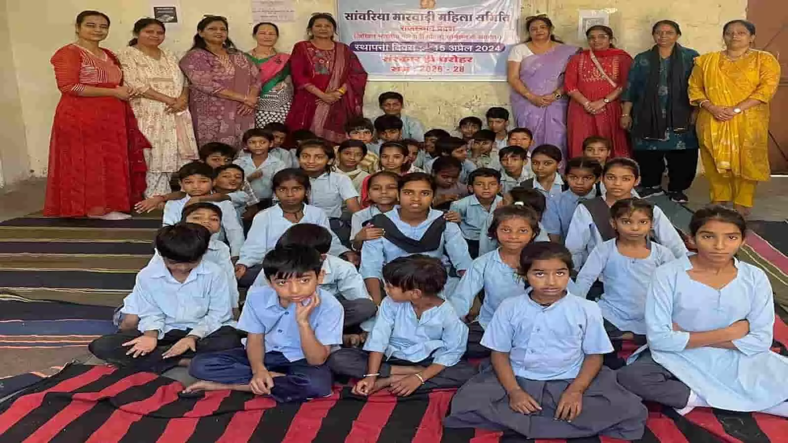 चित्तौड़गढ़ के स्कूल में संस्कार शिविर के दौरान दरी पर बैठे बच्चे और पीछे खड़ी समिति की महिला सदस्य।C