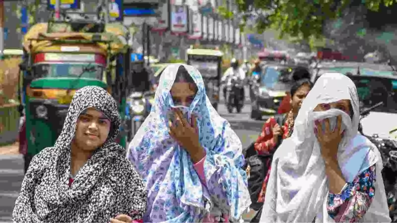दिल्ली की सड़क पर भीषण गर्मी के दौरान तीन महिलाएं कपड़े से चेहरा ढककर पैदल चल रही हैं।
