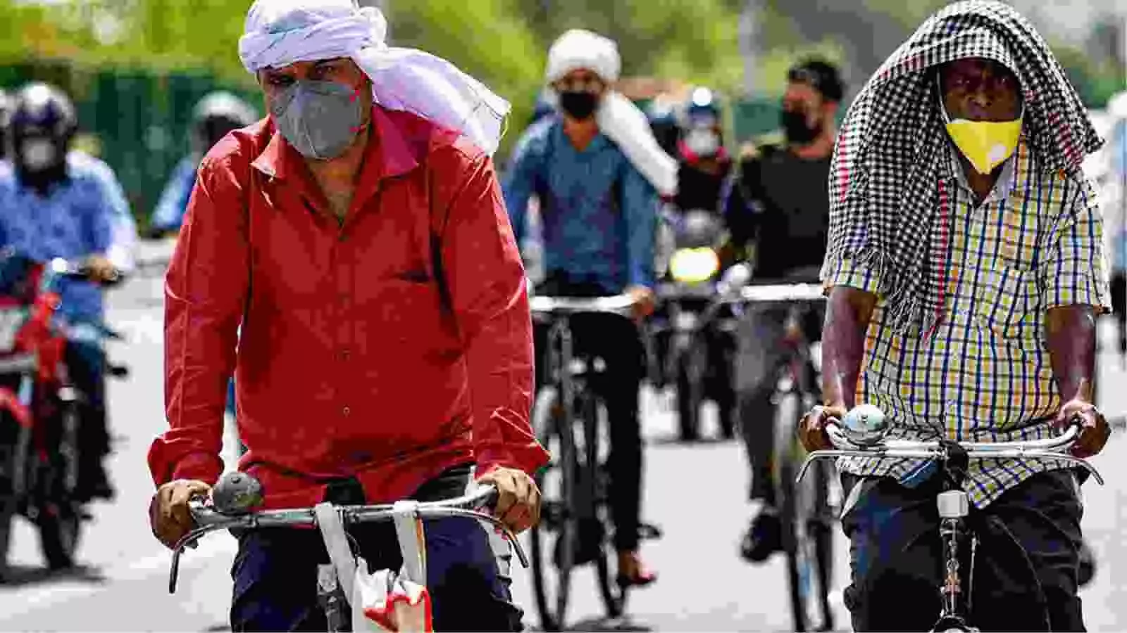 दिल्ली की सड़क पर तेज धूप में दो व्यक्ति साइकिल चलाते हुए कपड़े से चेहरा ढककर जा रहे हैं।