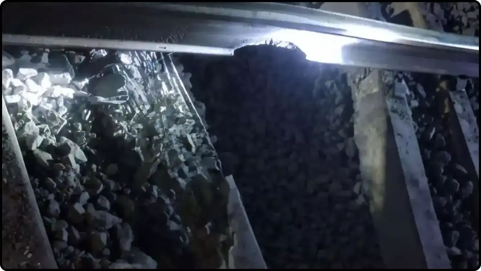 अंधेरे में टॉर्च की रोशनी में दिखाई दे रहा क्षतिग्रस्त रेलवे ट्रैक और बिखरे हुए पत्थर।