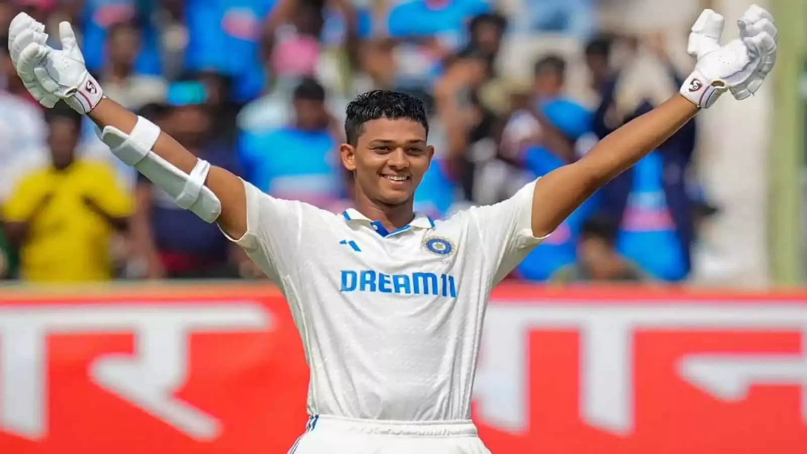 सफेद जर्सी पहने क्रिकेटर यशस्वी जायसवाल मैदान पर हाथ उठाकर शतक का जश्न मनाते हुए। सफेद जर्सी पहने क्रिकेटर यशस्वी जायसवाल मैदान पर हाथ उठाकर शतक का जश्न मनाते हुए।