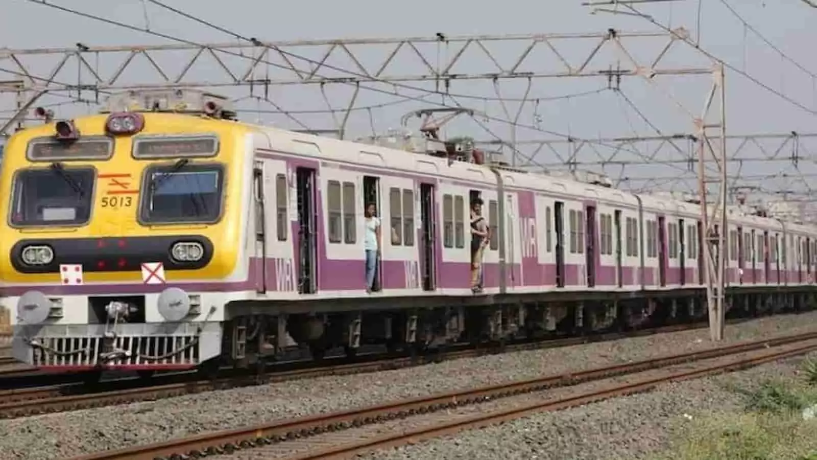 रेलवे ट्रैक पर चलती हुई मुंबई वेस्टर्न रेलवे की लोकल ट्रेन और बिजली के तार।