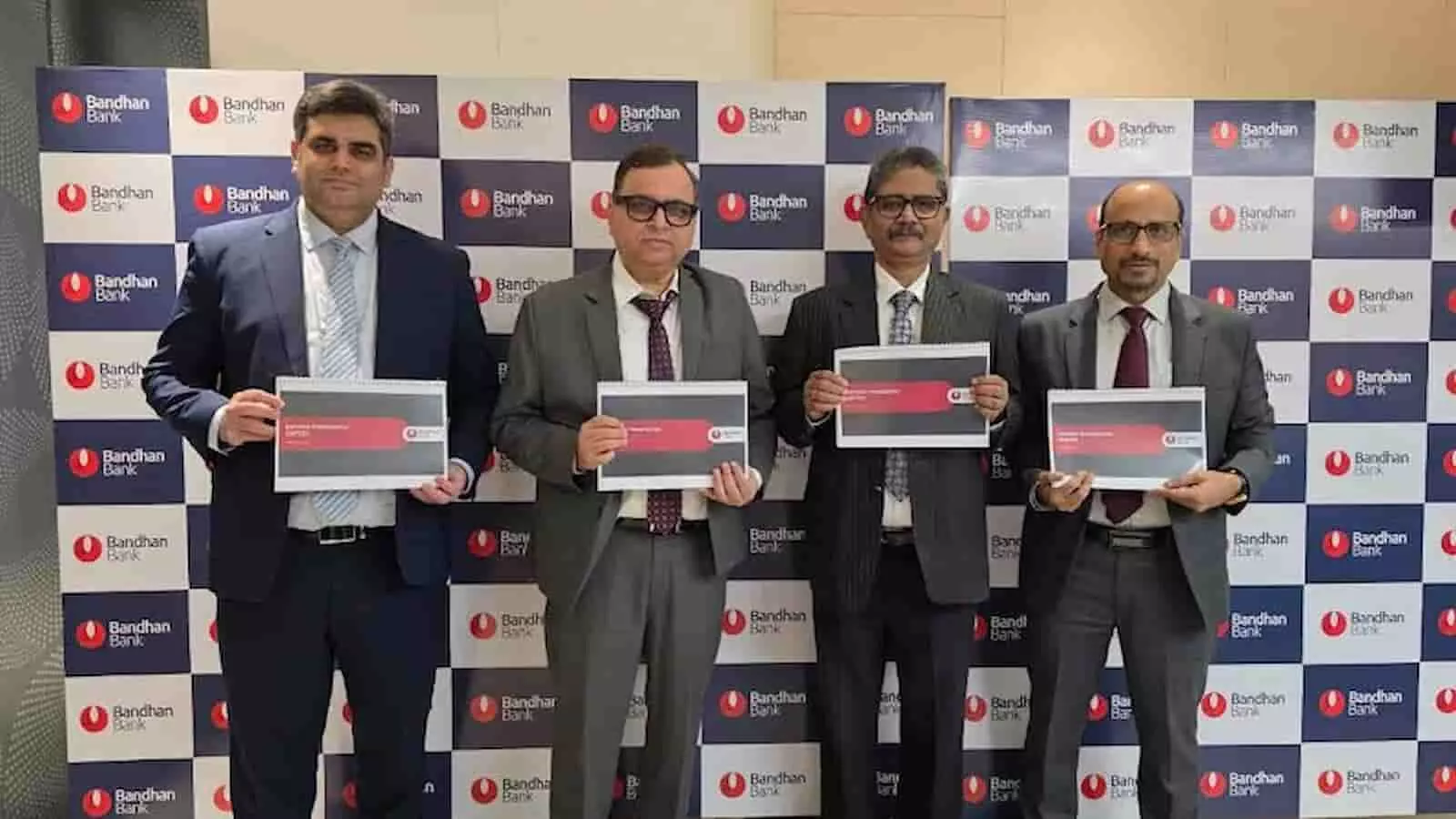 बंधन बैंक के अधिकारी वित्तीय परिणामों के दस्तावेज हाथ में लेकर बैंक के लोगो वाले बैकड्रॉप के सामने खड़े हैं। बंधन बैंक के अधिकारी वित्तीय परिणामों के दस्तावेज हाथ में लेकर बैंक के लोगो वाले बैकड्रॉप के सामने खड़े हैं।
