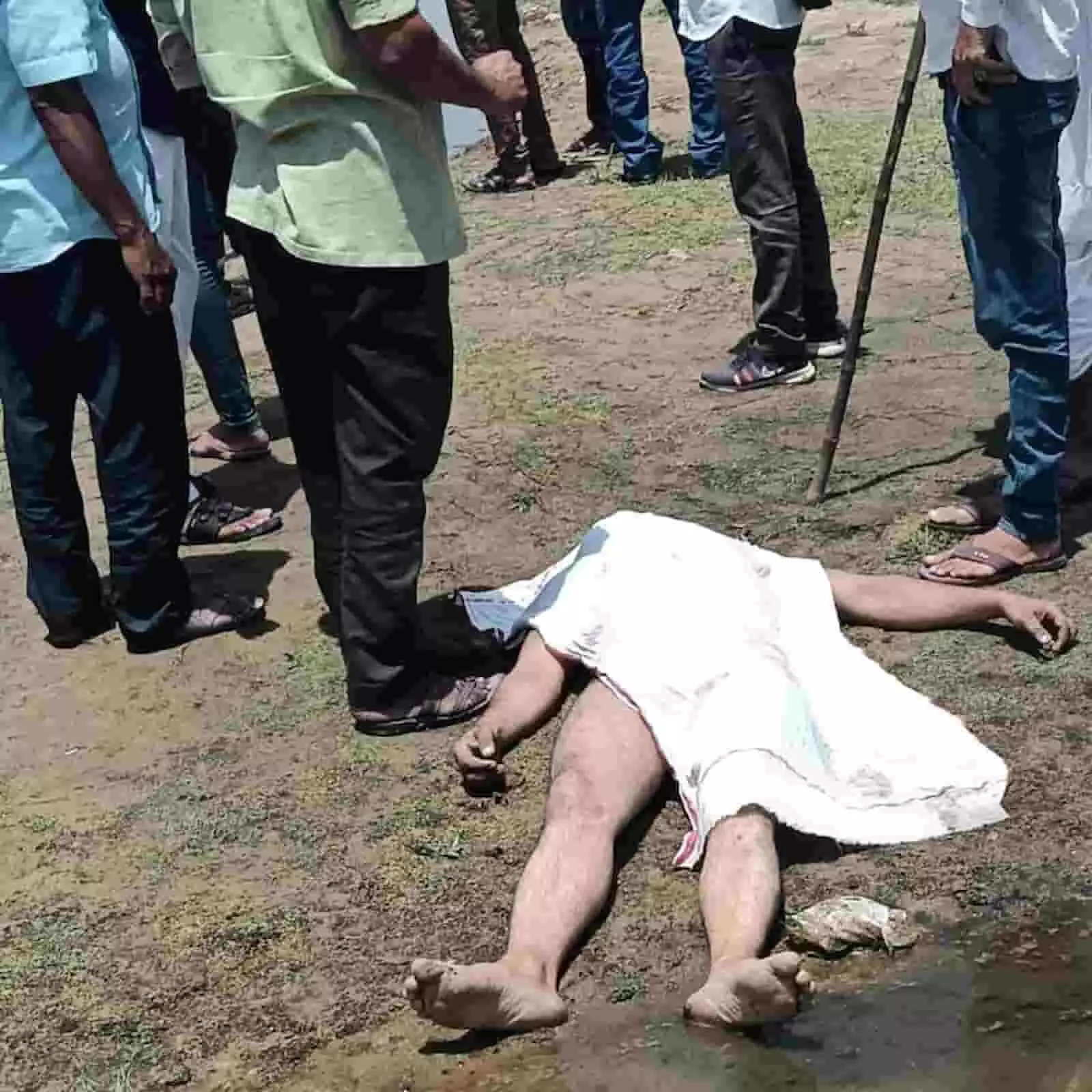 मोरेल नदी के किनारे जमीन पर ढका हुआ शव और आसपास खड़े ग्रामीण एवं पुलिसकर्मी। मोरेल नदी के किनारे जमीन पर ढका हुआ शव और आसपास खड़े ग्रामीण एवं पुलिसकर्मी।