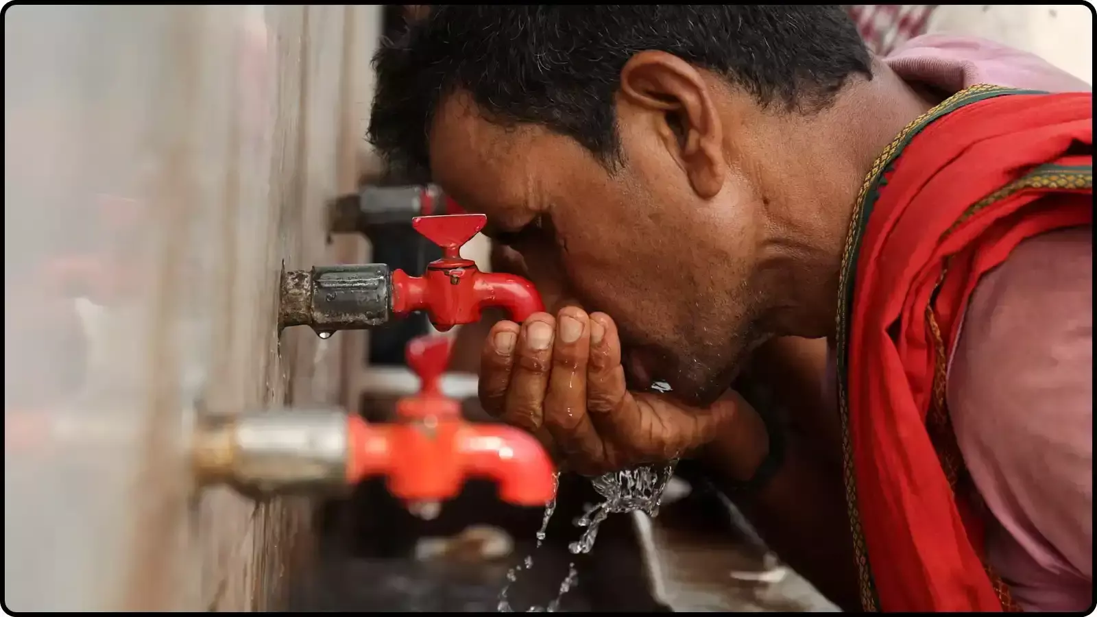 सार्वजनिक स्थान पर लगे लाल रंग के नल से हाथों में पानी लेकर पीता हुआ एक व्यक्ति। सार्वजनिक स्थान पर लगे लाल रंग के नल से हाथों में पानी लेकर पीता हुआ एक व्यक्ति।