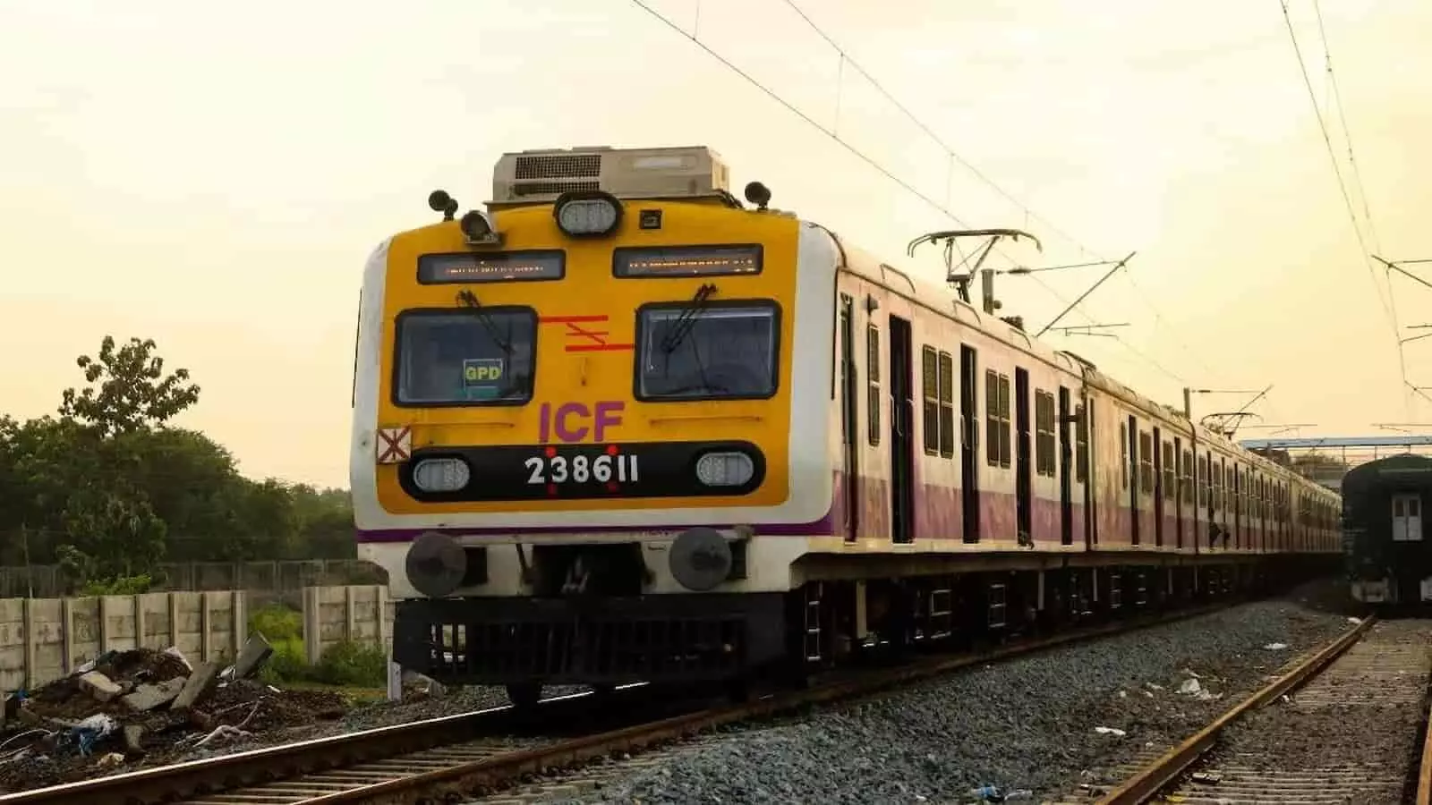 रेलवे ट्रैक पर चलती हुई पीली और सफेद रंग की भारतीय रेलवे की लोकल ट्रेन का दृश्य।